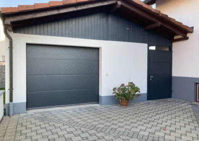 Modernes Garagentor mit passender Nebentür in Grau an einem weißen Haus – Außengestaltung von der Schreinerei Kappus aus Ettenheim